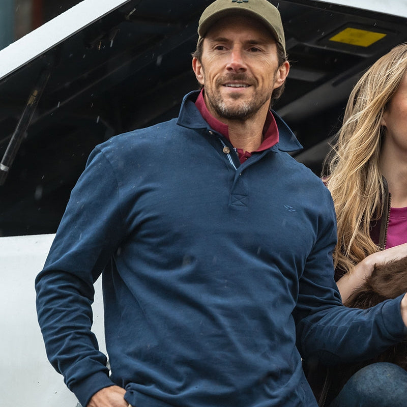 Man wearing a blue sweater and cap standing next to a white vehicle with a woman beside him.